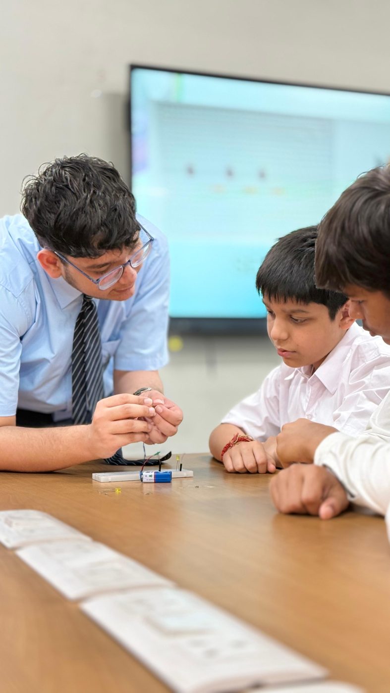 A mentor guiding two students through a hands-on electronics circuit exercise